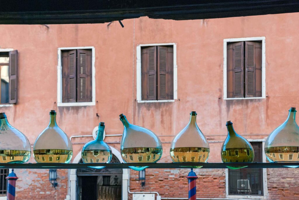 Row of glass bottles half filled with water showing reflection of Venice water canal